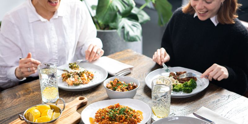 This is an image of two women laughing and enjoying plated up Nourish'd meals
