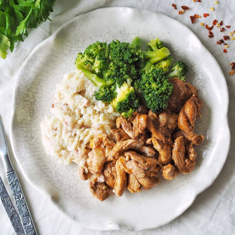 Plate with cooked broccoli, seasoned chicken pieces, and creamy mashed potatoes arranged in sections.