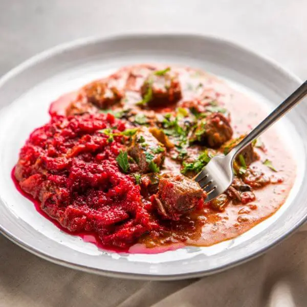 An action shot of Beef Stroganoff, highlighting a fork lifting a piece of tender beef from the plate. The dish, garnished with chopped spring onions, sits on a dark grey benchtop, with a comforting and creamy texture that invites a bite.